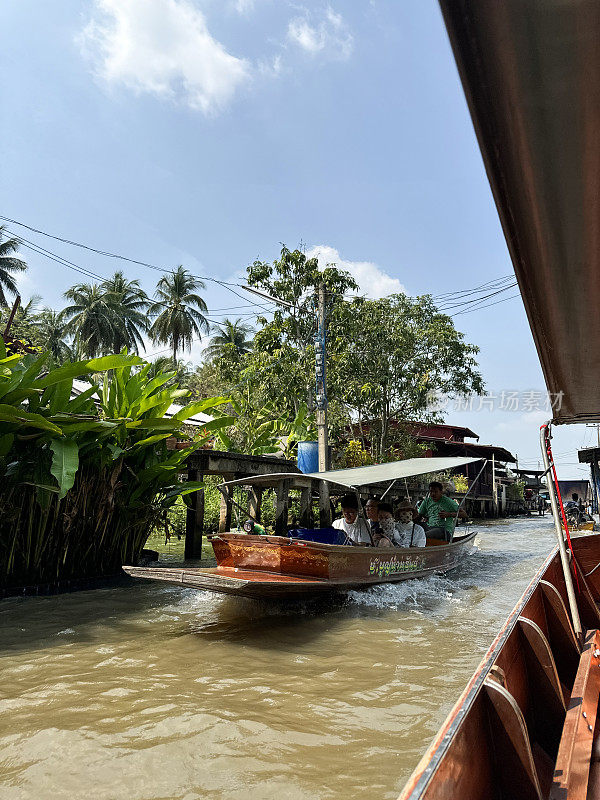 一艘带顶篷的木船载着游客在Khlong Damnoen Saduak运河附近游览，游船行驶在通往Tha Chin和Mae Klong河的水路上